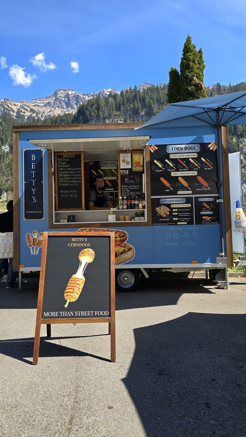 Betty's Corn Dogs blue food trailer in Lauterbrunnen with Swiss Alps and waterfall behind